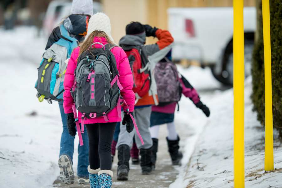 Kids wearing multi-colored coats and boots walk home from school in the winter.