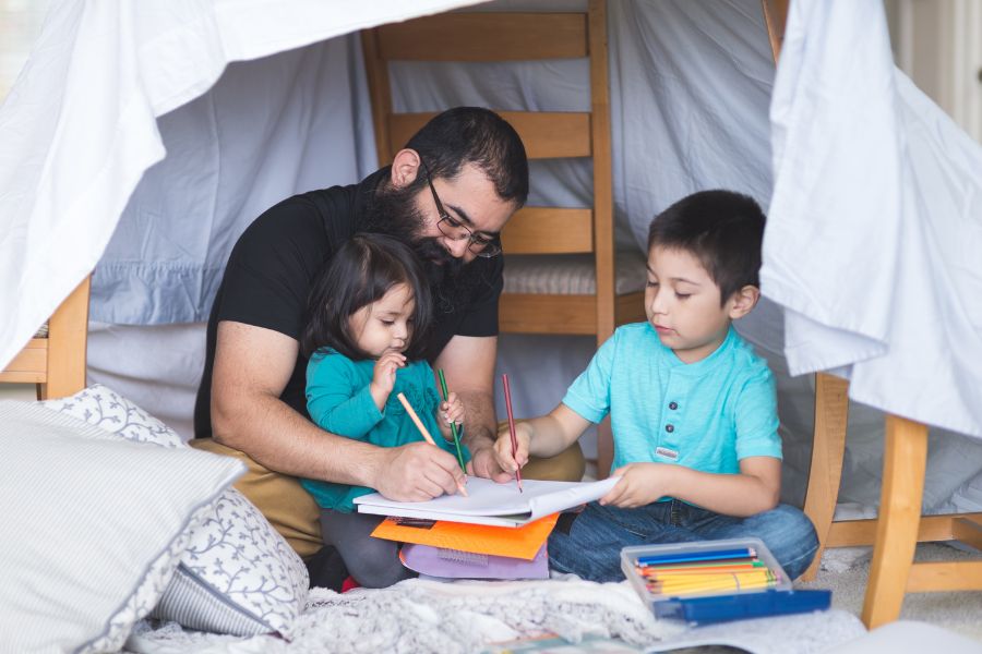 A father sits with his kids in a homemade fort